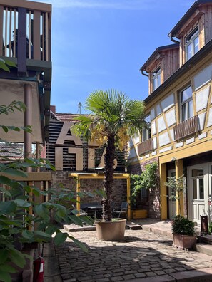 Ein Innenhof mit Kopfsteinpflaster, einer Palme und einem Gebäude mit gelber Fassade und einem Schild mit der Aufschrift 'WIKO'.