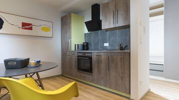 A compact kitchen with wooden cabinets, a built-in oven, and a small dining area with a yellow chair.