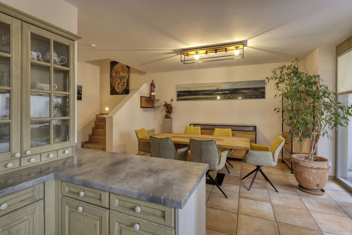 Una cocina moderna con encimera de granito, un comedor con mesa y sillas de madera, y una escalera que sube a un nivel superior.