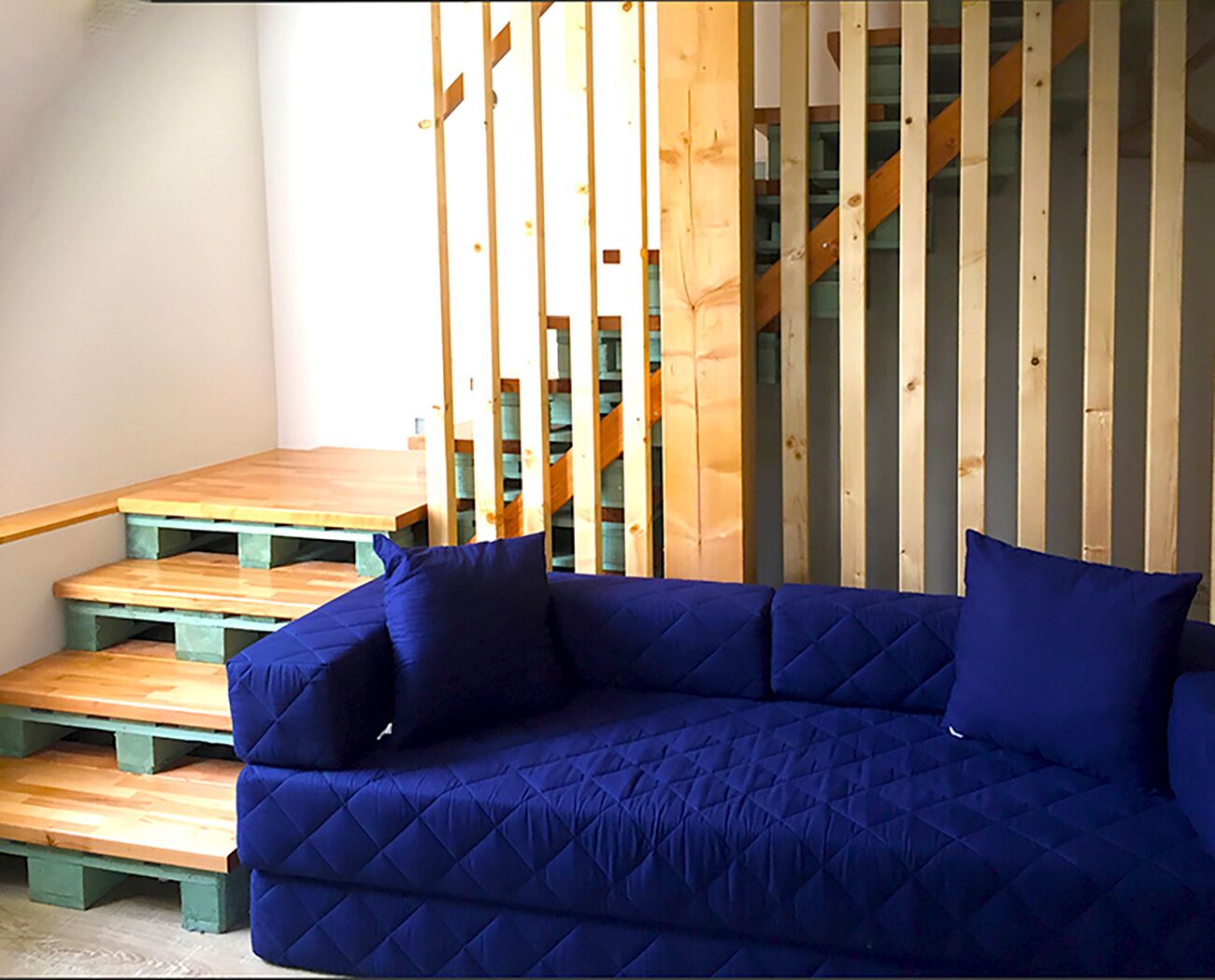 A blue sofa with cushions, a wooden bench, and a staircase with wooden railings.