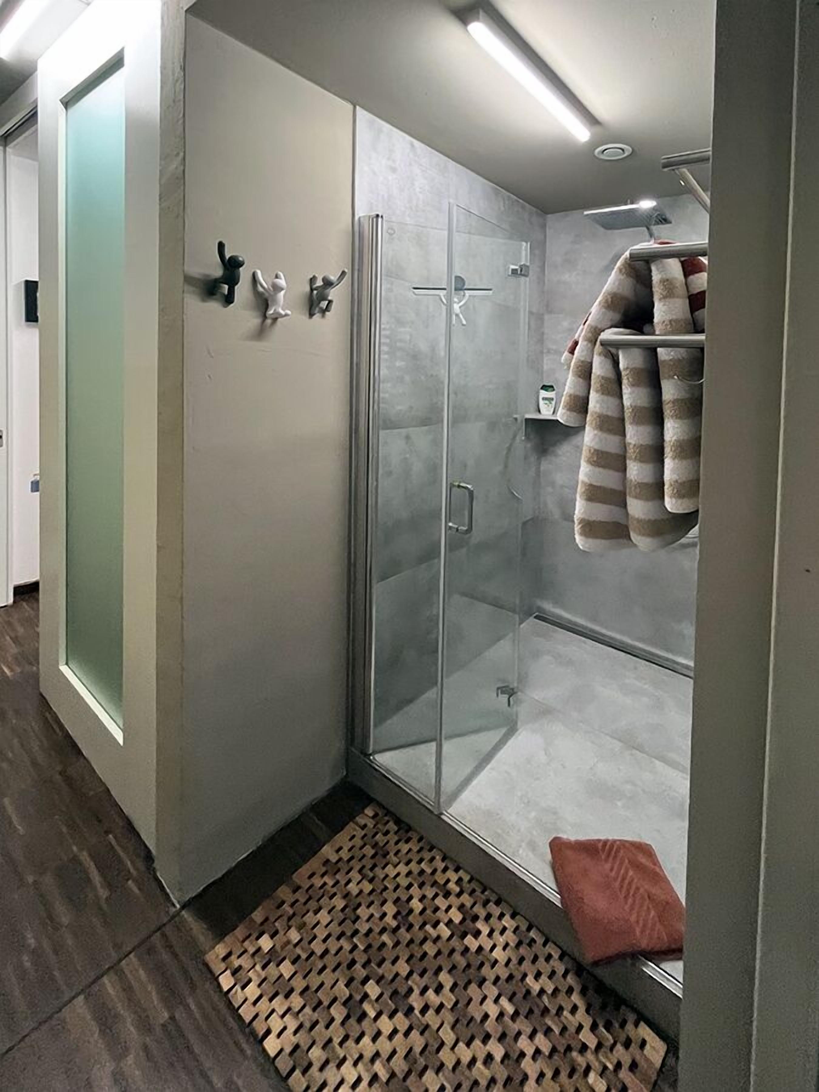 A modern bathroom with a glass shower enclosure, a towel rack, and a patterned rug.