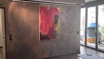 A modern interior with a large abstract painting on a textured wall, a sliding glass door leading to an outdoor area, and a minimalist table with a wire basket.