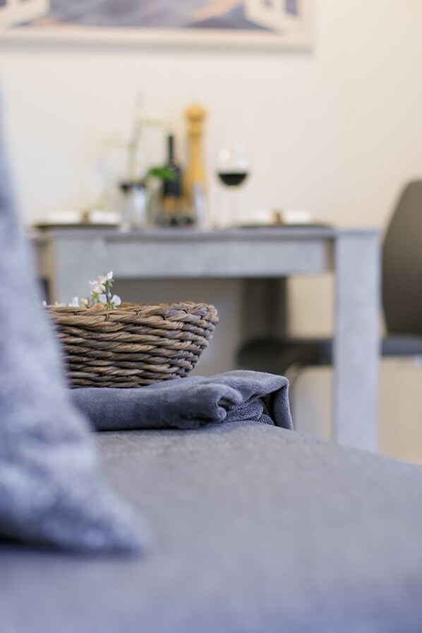 Ein Korbwesenkorb auf einem grauen Sofa, im Hintergrund verschwommen eine Tafel mit einer Flasche und Gläsern.