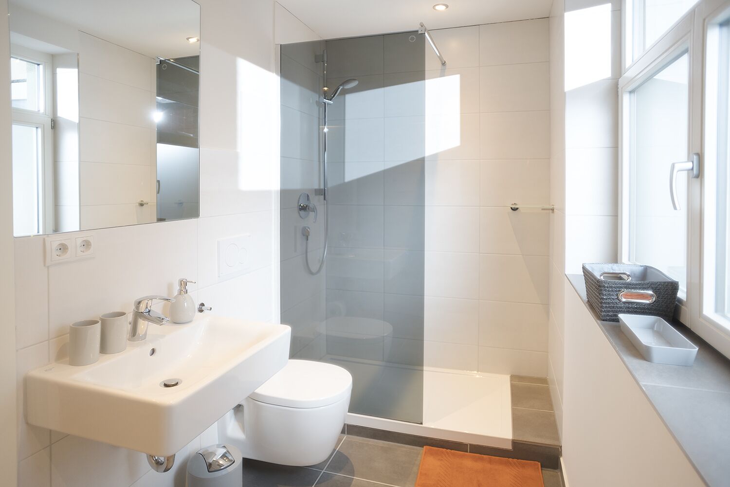 Un baño moderno con cabina de ducha de vidrio, un lavabo blanco y un inodoro.