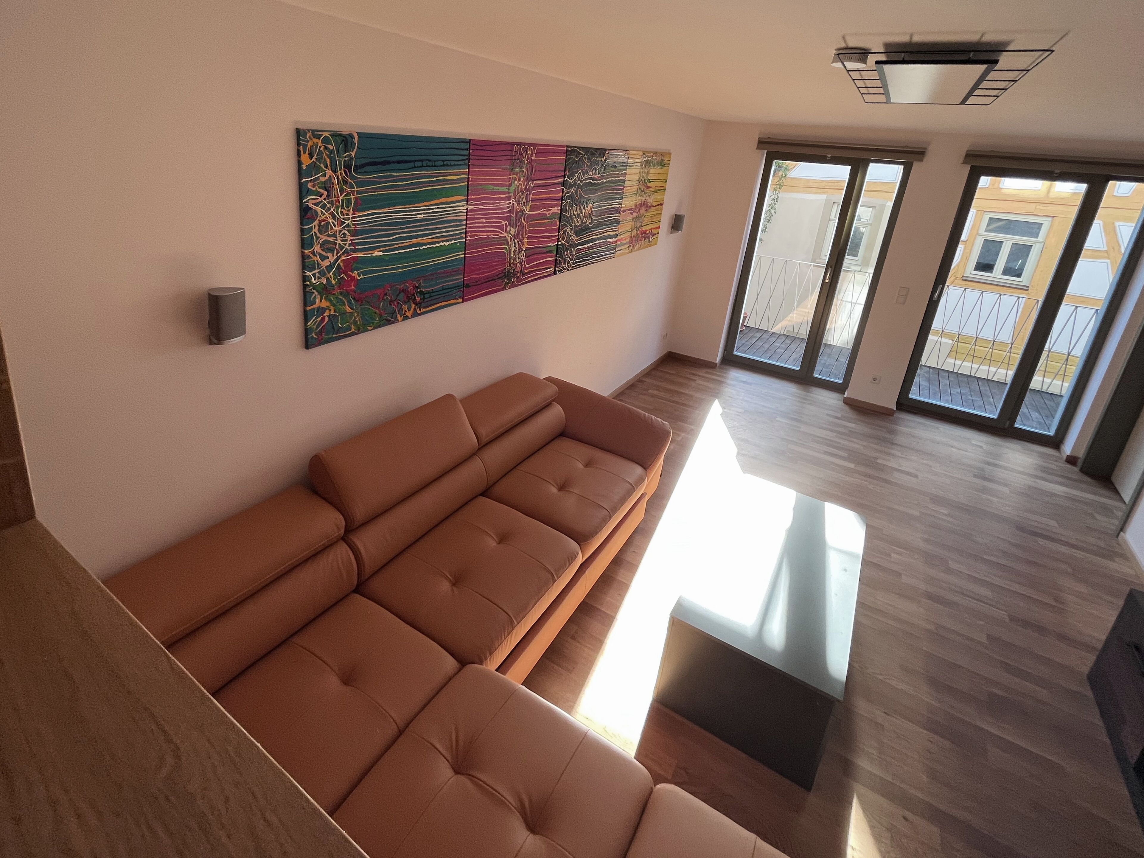 A modern living room with a sectional sofa, a colorful abstract painting, and a view of the outside balcony.