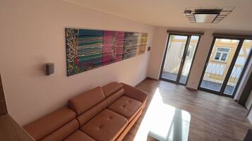 A modern living room with a sectional sofa, a colorful abstract painting, and a view of the outside balcony.