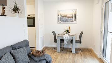 A compact living space with a dining area, a sofa, a table with chairs, a plant, and a painting on the wall.