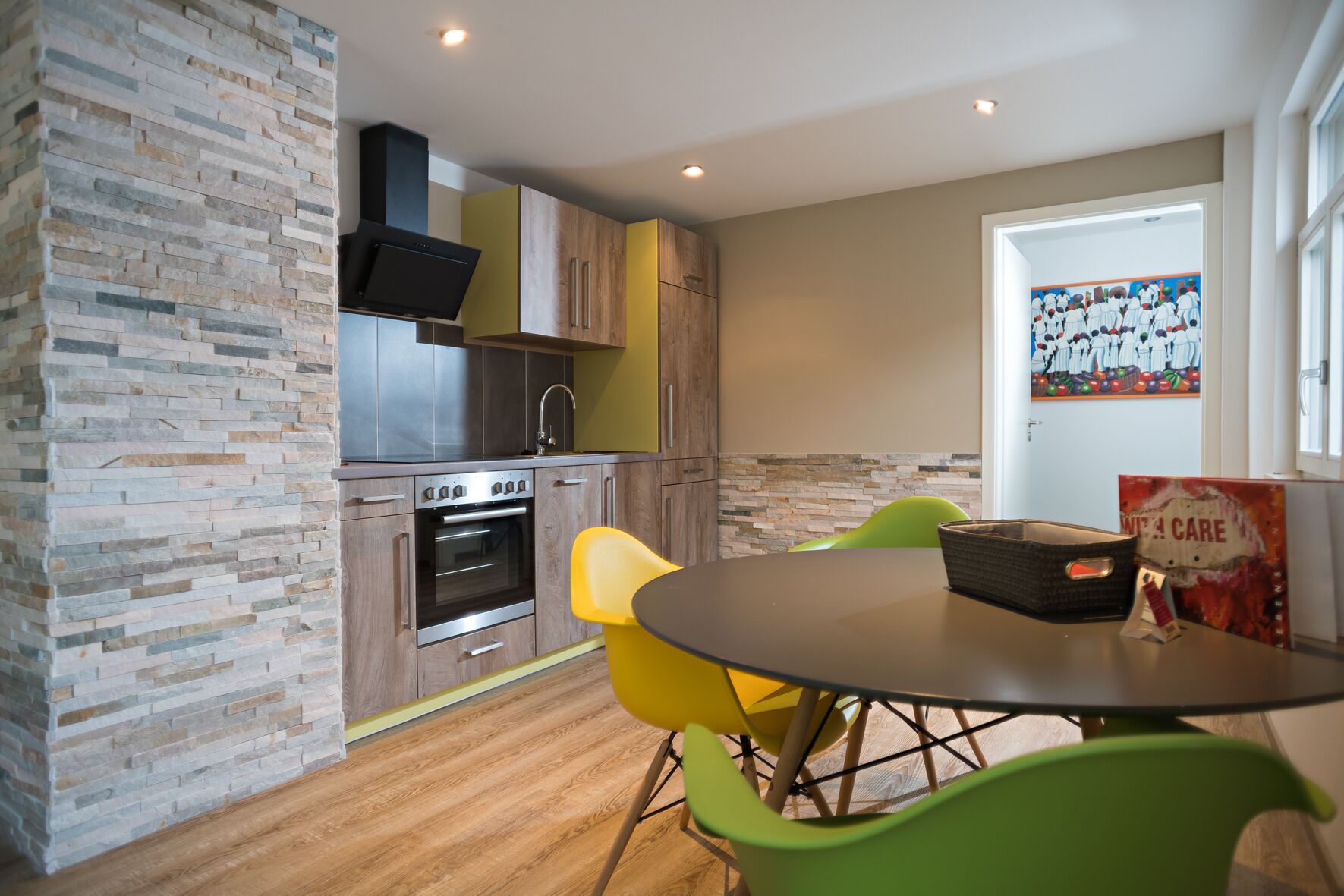 Une cuisine moderne avec un revêtement mural en pierre, des appareils en acier inoxydable et un coin repas comprenant une table ronde et des chaises vertes.