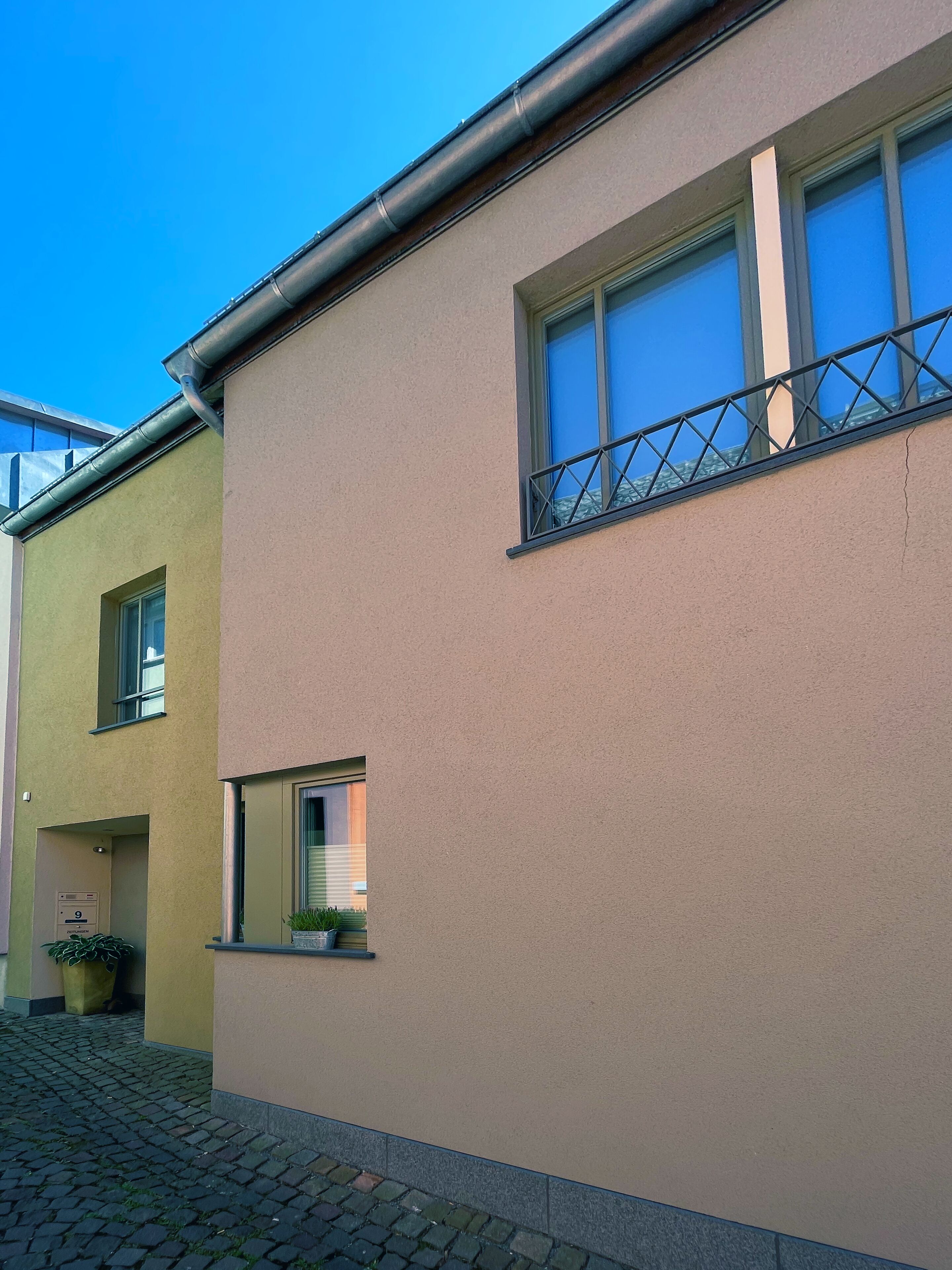 Ein Gebäude mit einer beigefarbenen Fassade, einem Fenster mit Metallgitter und einem Blumentopf im Erdgeschoss.