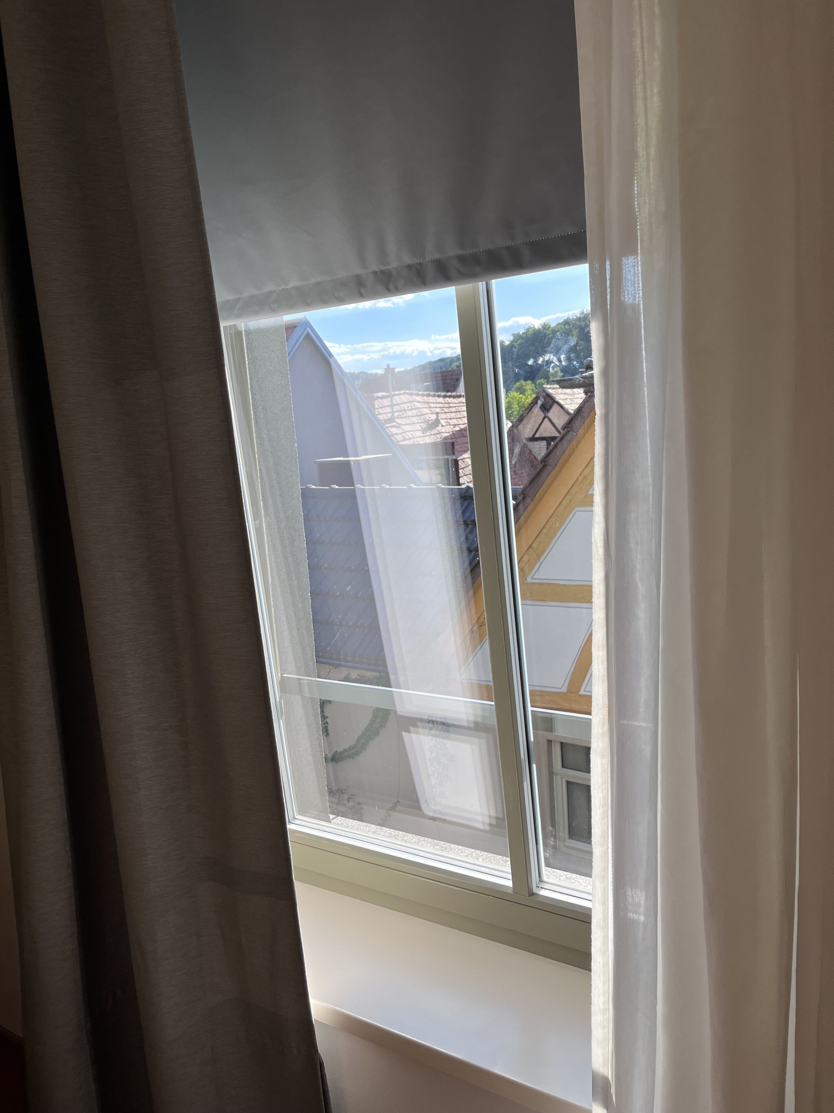 A window with a view of a building's roof and a clear sky.