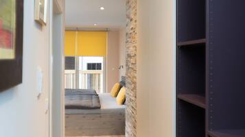A modern hallway with a wooden floor, a stone accent wall, and a bed with yellow pillows.