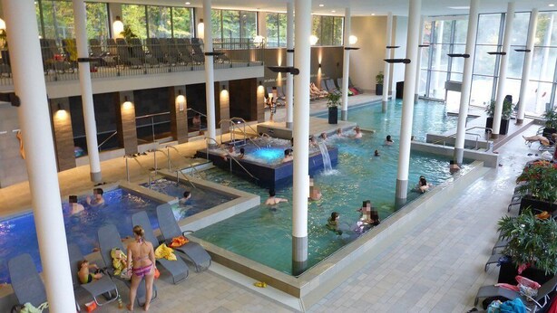 Una gran piscina interior con varios niveles, zonas de descanso y una bañera de hidromasaje.