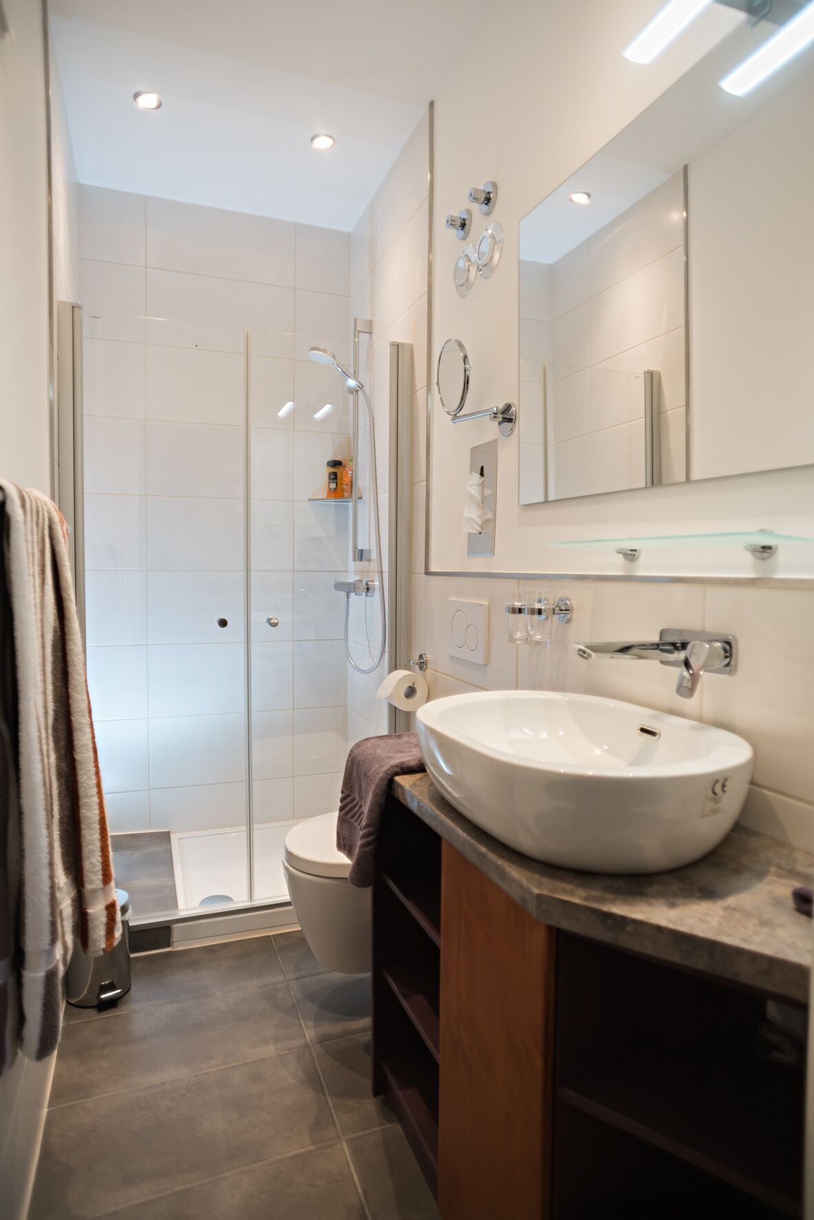 Ein modernes Badezimmer mit einer gläsernen Duschkabine, einem weißen Waschbecken und einem großen Spiegel.