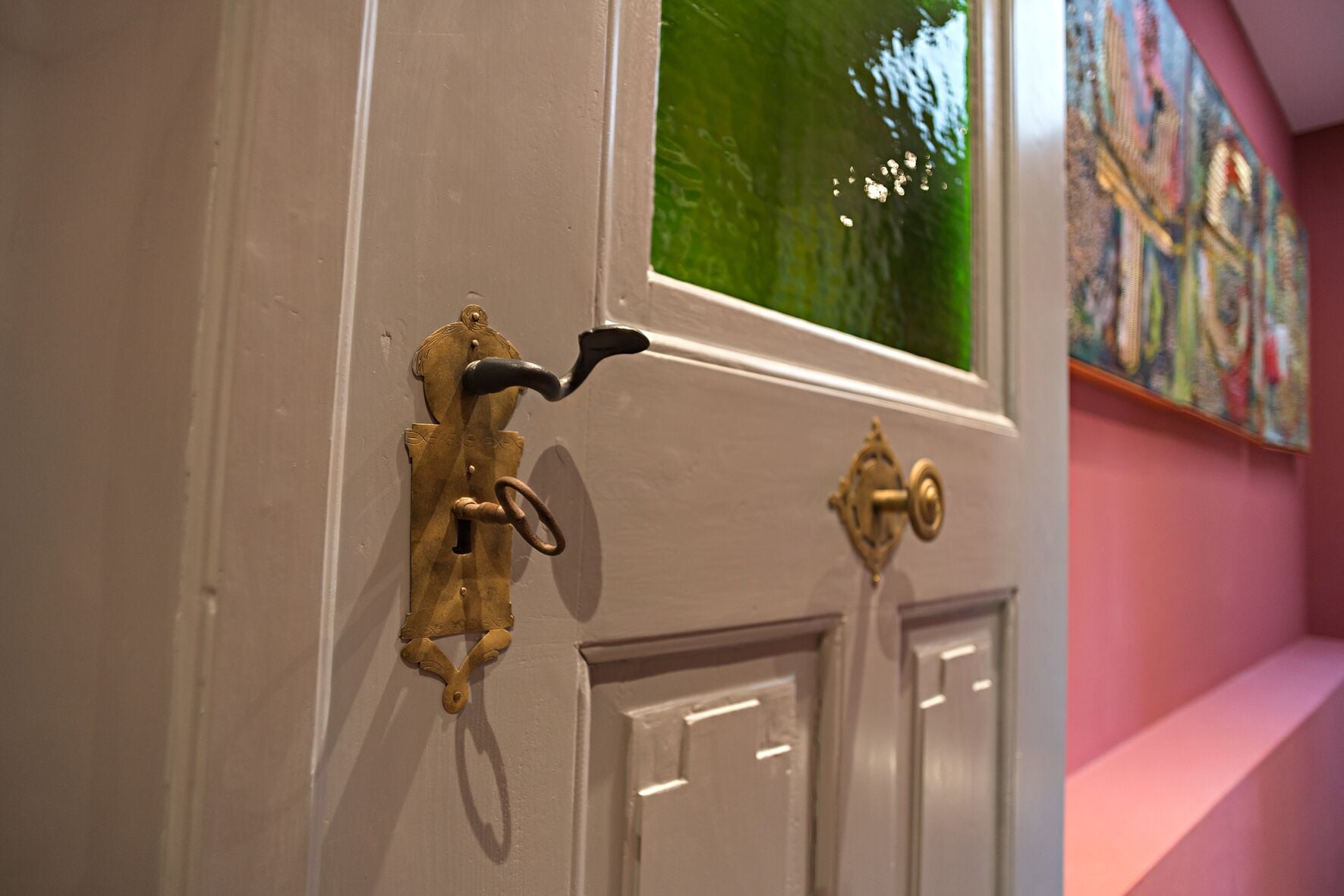 Une porte dotée d’une poignée en laiton ancien et une fenêtre donnant sur un paysage verdoyant.