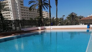 En klar, blå swimmingpool med gelænder i metal, omgivet af palmer og bygninger i baggrunden.