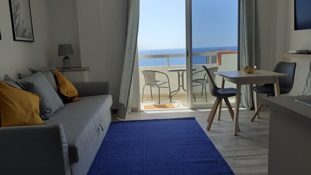 Et moderne værelse med balkon, sofa, spisebord og TV.