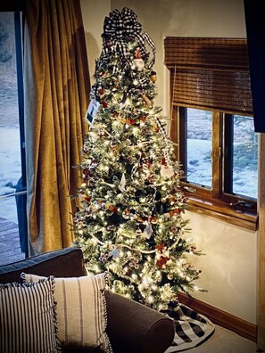 A decorated Christmas tree in a living room with a window and curtains.