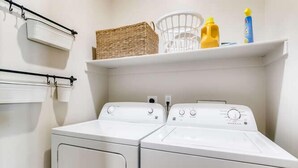 A laundry area with two white front-loading washers and dryers, a white shelf with baskets and cleaning supplies, and a white wall-mounted drying rack. - Family Hot Tub, MountainScape Chalet! Paradise! (Breckenridge)