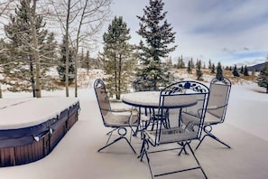 A snow-covered patio with a round table and chairs, surrounded by trees.