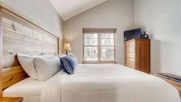 A bedroom with a bed, wooden headboard, a window, a dresser, and a television.
