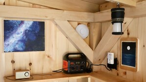 A wooden cabin interior with a radio, a telescope, and a framed picture of the night sky. - Tiny Cabin on Blue Hill Farm (Blue Hill)