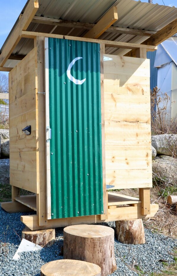 A wooden structure with a green door, a crescent moon symbol, and a metal roof.