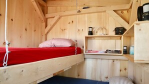 A compact wooden cabin with a bunk bed, a small shelf with books and a kettle, and a simple wooden structure. - Tiny Cabin on Blue Hill Farm (Blue Hill)