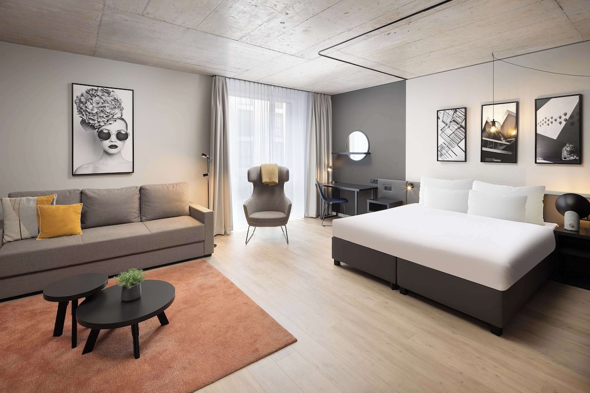 A modern hotel room with a sofa, a bed, a desk, and a chair.