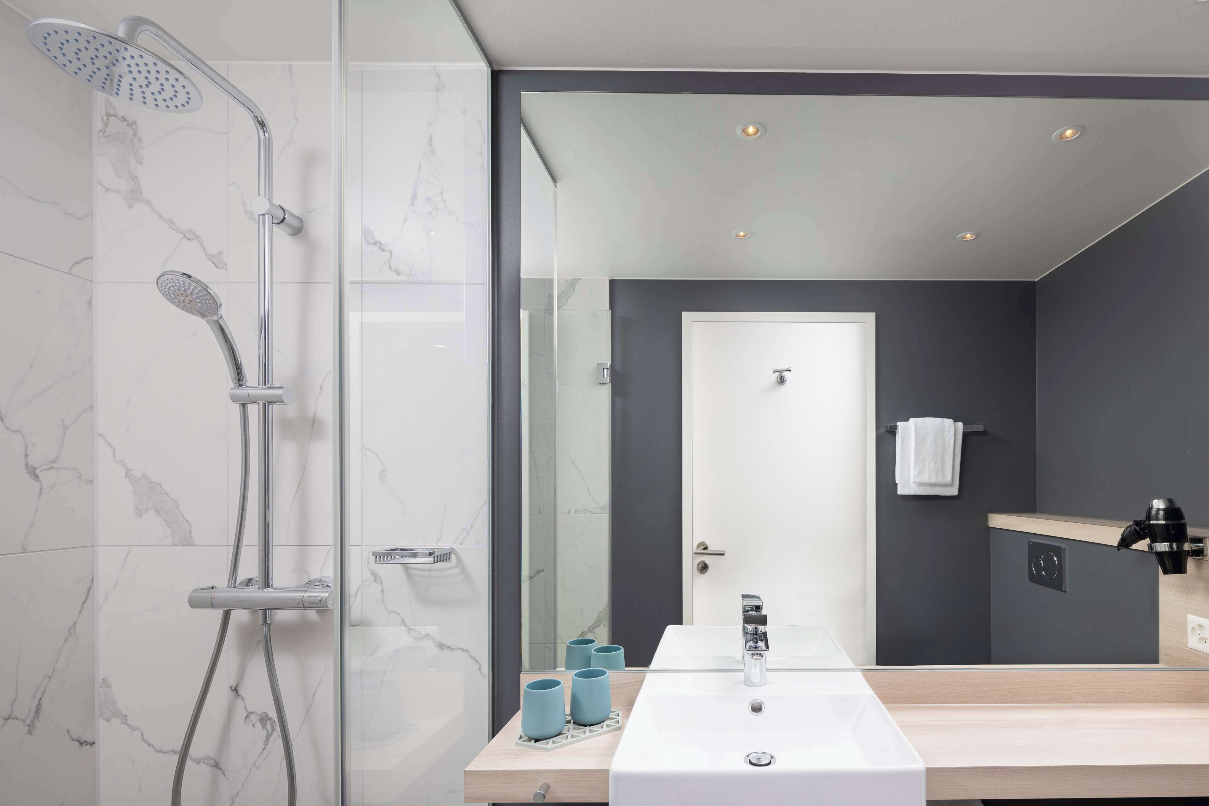 Un baño moderno con ducha de vidrio, un lavabo blanco y un espejo que refleja el ambiente.