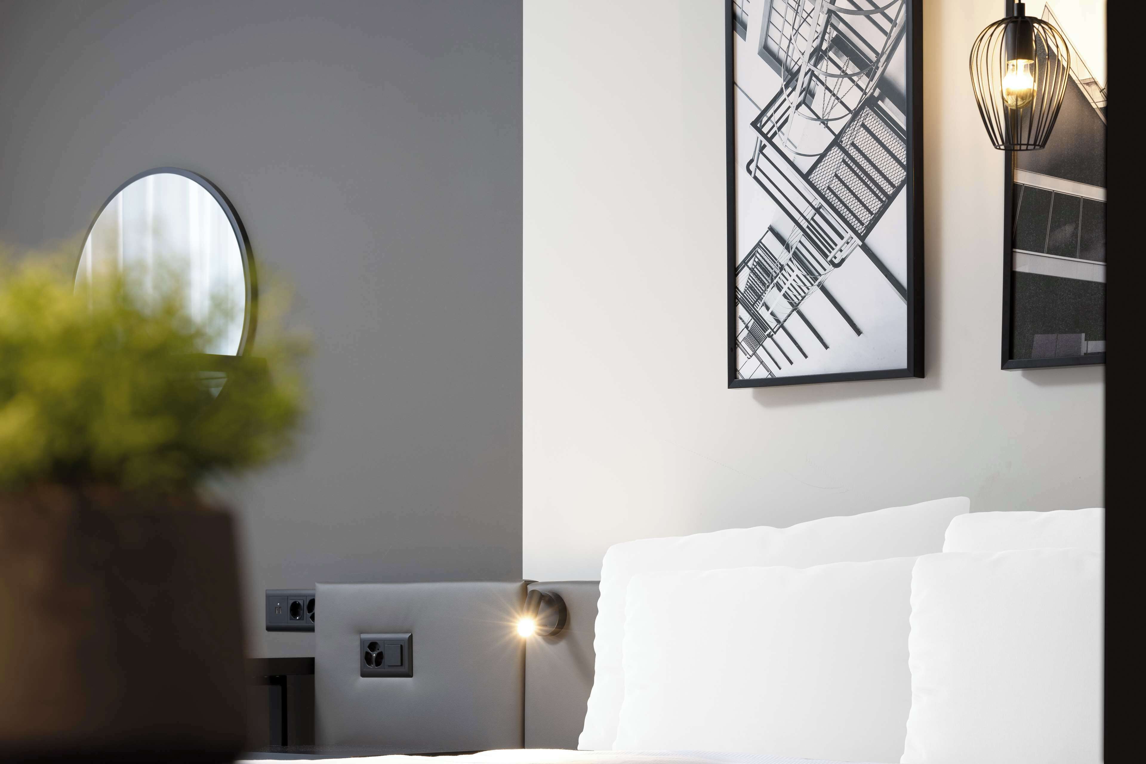 A hotel room with a bed, a large window, and a framed cityscape picture on the wall.