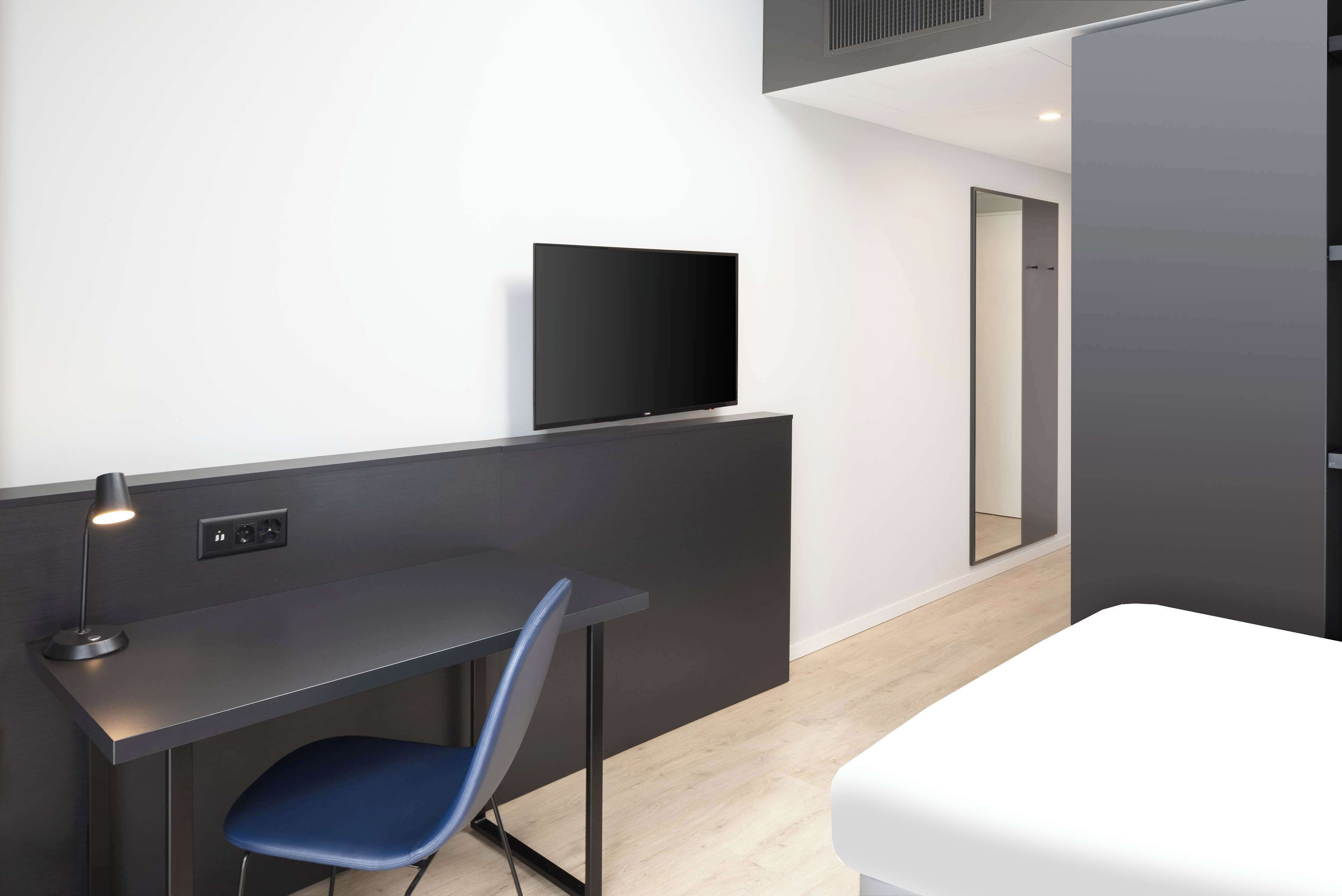 A modern hotel room with a desk, chair, and a flat-screen TV.
