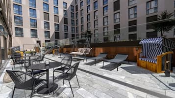 Une terrasse sur le toit avec un espace extérieur aménagé, comprenant des tables et des chaises, ainsi qu’un petit espace piscine.