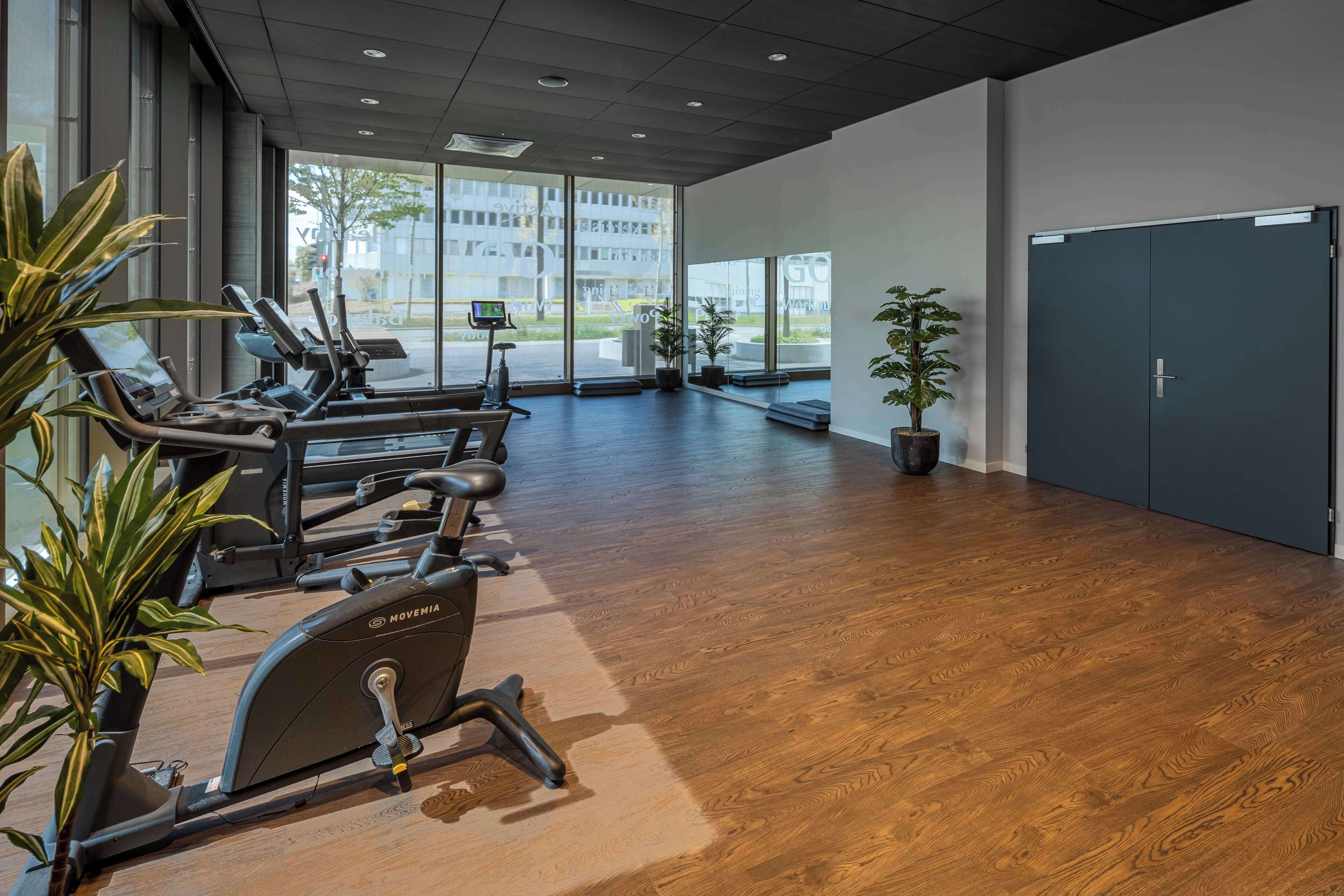 A gym with exercise equipment, large windows, and wooden flooring.