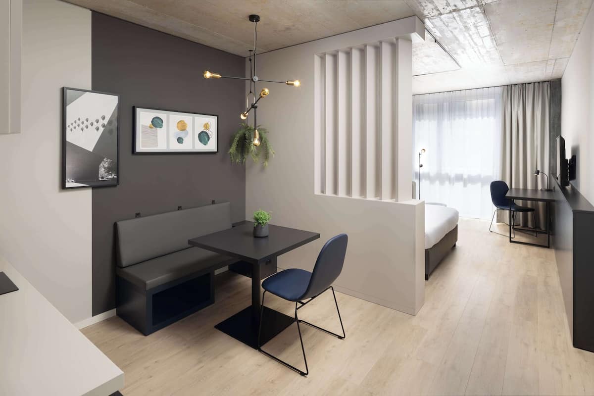 A modern, well-lit room with a dining table, chairs, a bench, a small potted plant, and a large window with curtains.