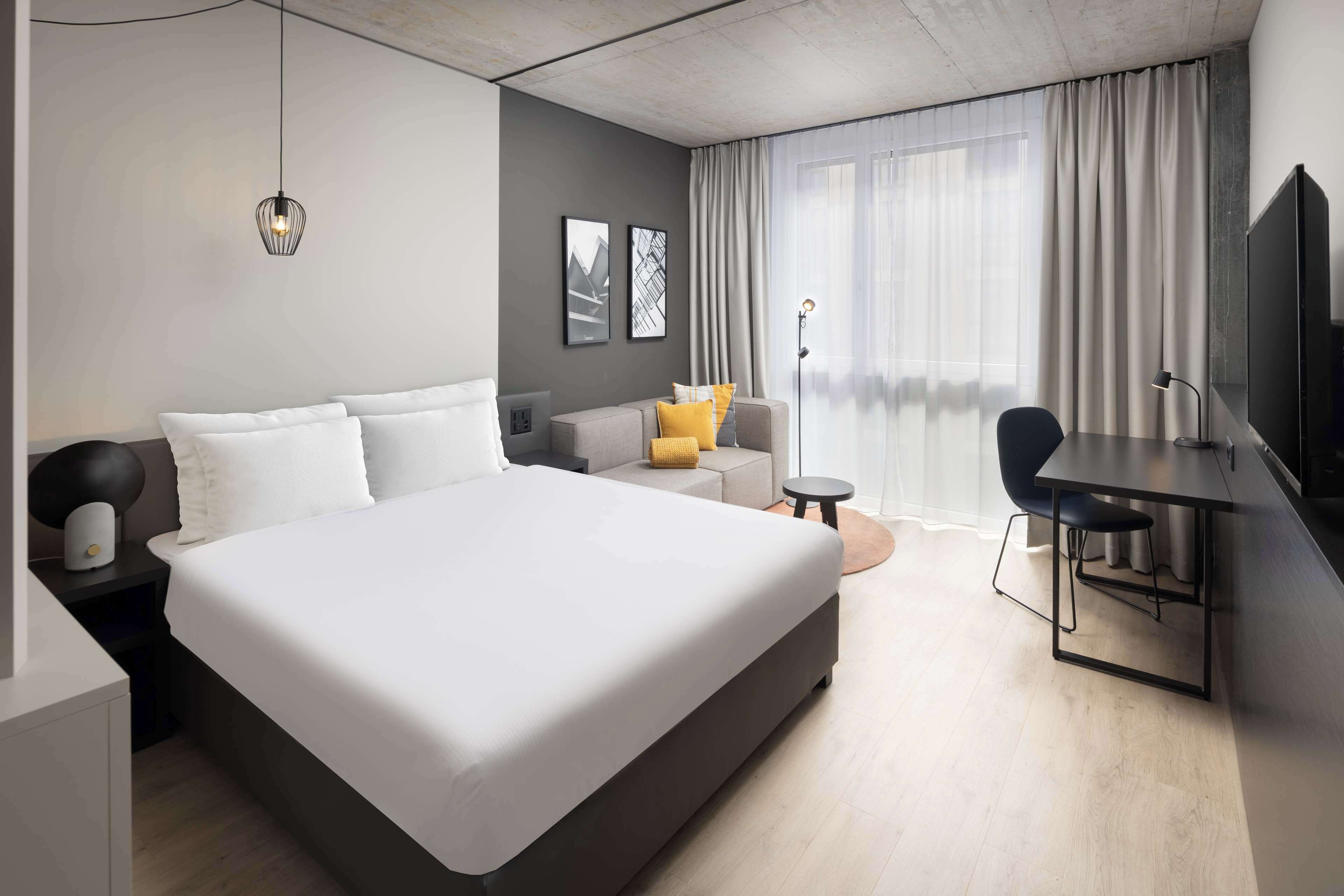 A modern hotel room with a large bed, a desk, a chair, and a TV.
