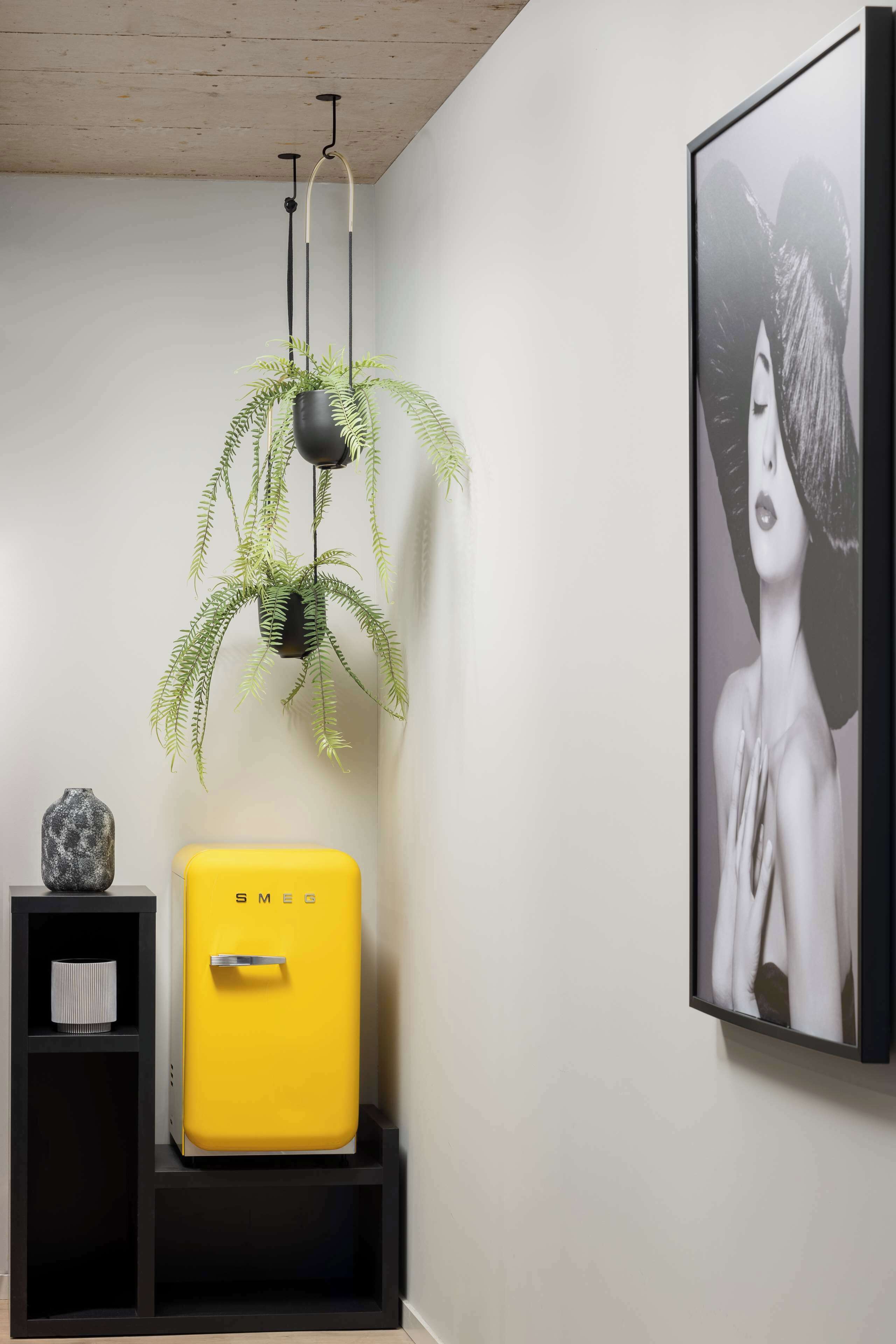 Een kamer met een gele koffer, een potplant, een ingelijste afbeelding en een zwarte plank met een vaas.