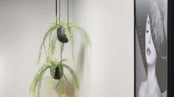 Una habitación con una maleta amarilla, una planta en maceta, una obra de arte enmarco y un estante negro con un jarrón.