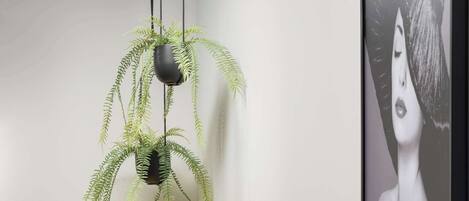 Una habitación con una maleta amarilla, una planta en maceta, una obra de arte enmarco y un estante negro con un jarrón.