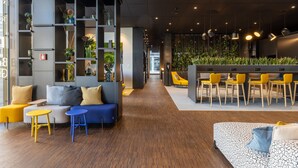 A modern interior with a central seating area, a long corridor, and a dining area with yellow chairs. - Radisson Hotel & Suites Zurich (Opfikon)
