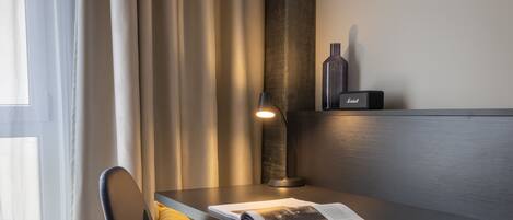 A modern room with a dark wooden desk, a lamp, a magazine, and a small speaker on the wall.