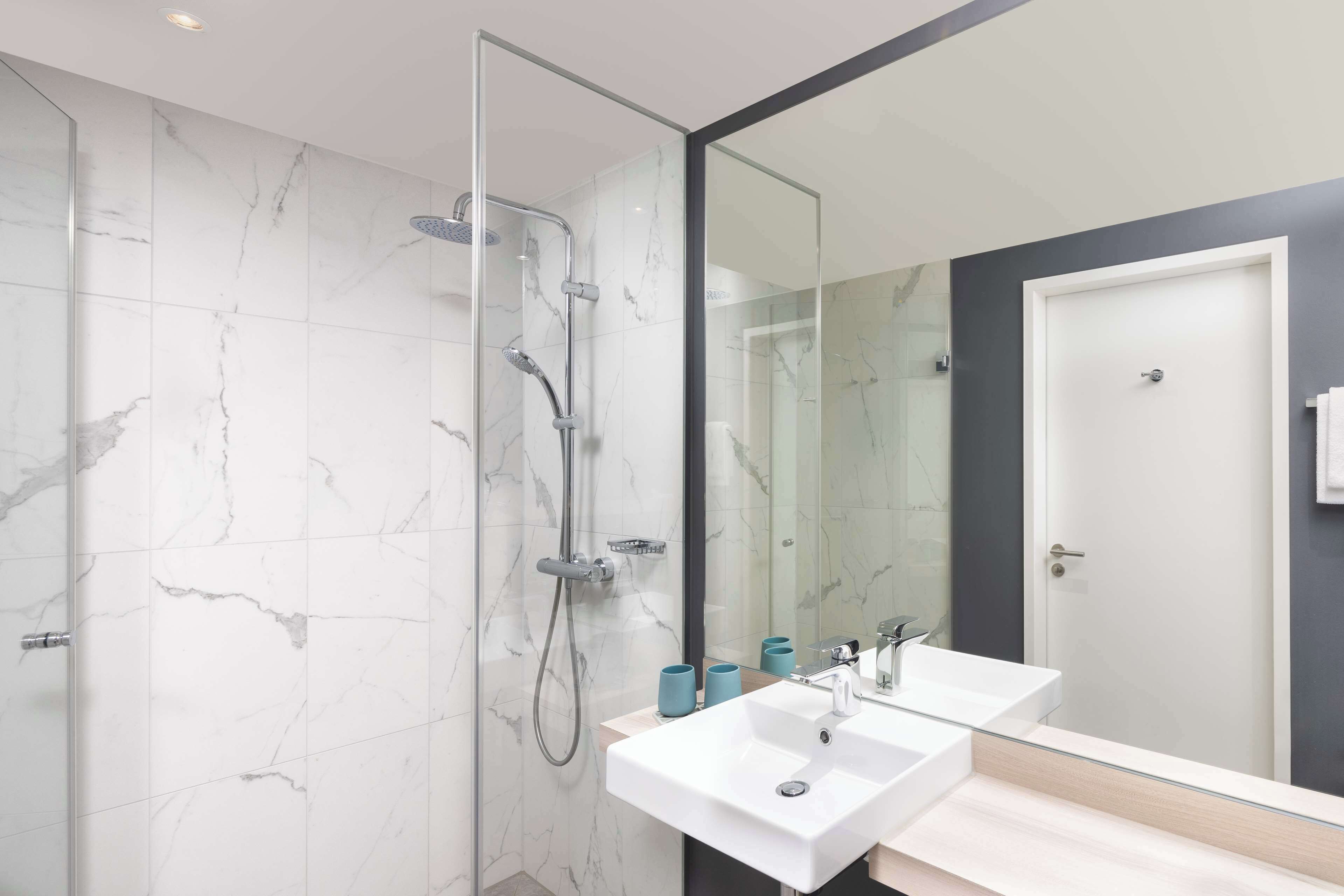 Un baño moderno con ducha de vidrio, dos lavamanos blancos y un espejo grande.