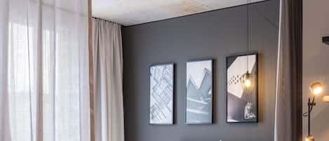 Une chambre à coucher moderne avec un grand lit, une table de chevet, une lampe sur pied et des œuvres d’art accrochées au mur.
