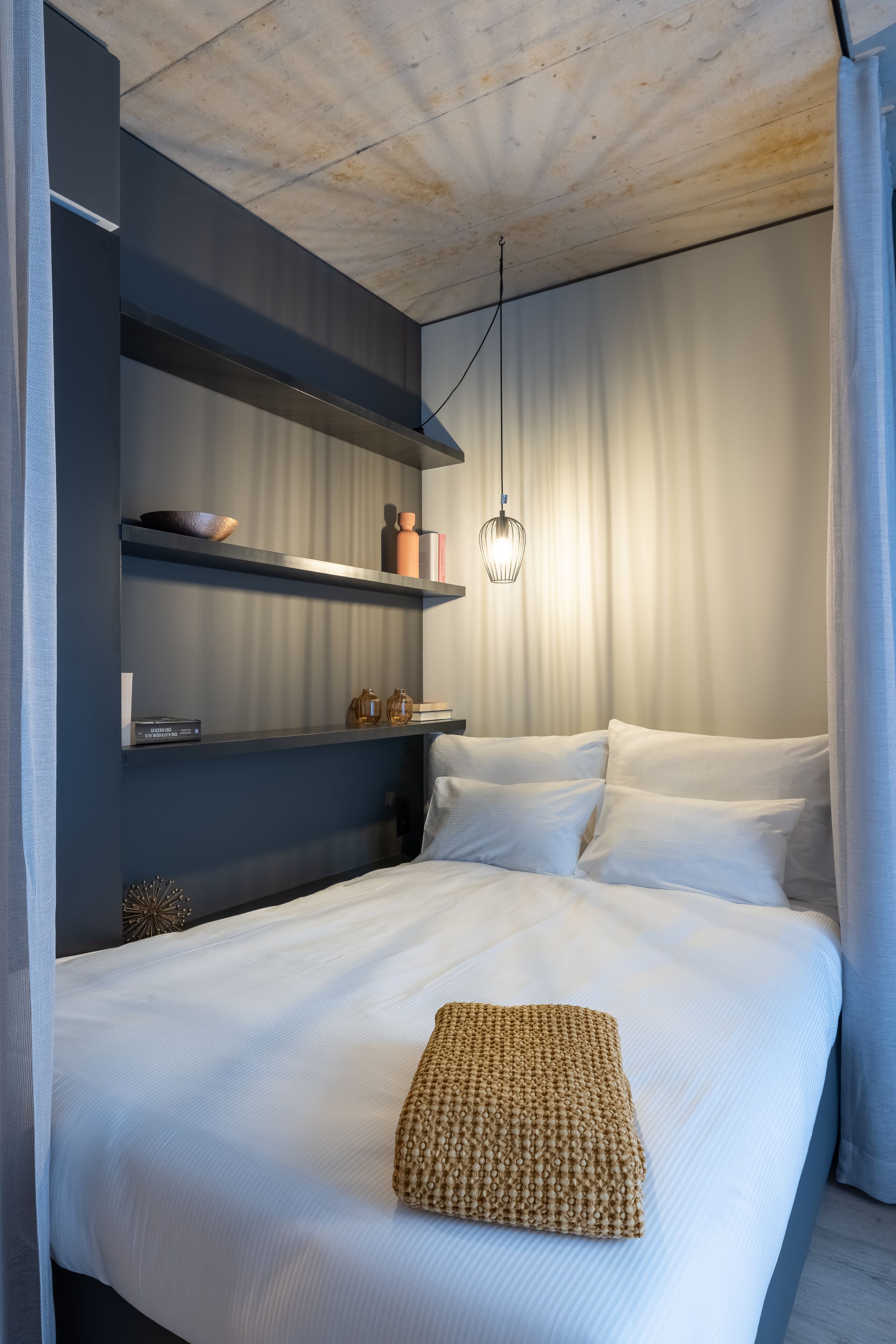 Una camera da letto moderna con un letto rifatto, uno scaffale con oggetti decorativi e un lampadario.