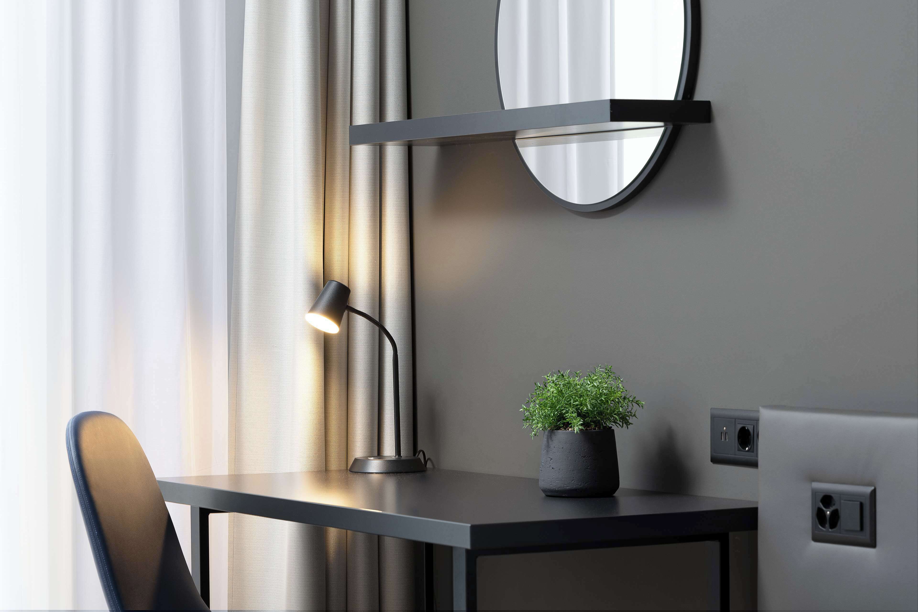 Un bureau moderne, agrémenté d’une lampe, d’une plante en pot et d’un miroir accroché au mur.
