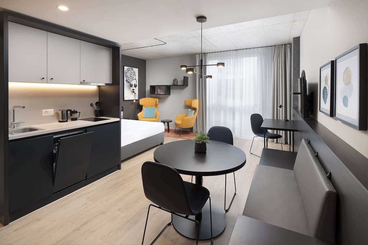 A modern hotel room with a kitchen, dining area, and seating space.