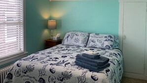 A bedroom with a bed, a nightstand, and a window with blinds. - Rustic Rooftop Delight - Bay Front 2 Bedroom Apts by RedAwning (Norfolk)