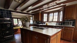 A kitchen with wooden cabinets, a large island, a built-in oven, and a microwave. - Rockport Home with Beautiful Ocean Views (Rockport)