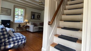 A staircase with wooden steps and a handrail, leading to a landing area with a view of a living room. - Rockport Home with Beautiful Ocean Views (Rockport)