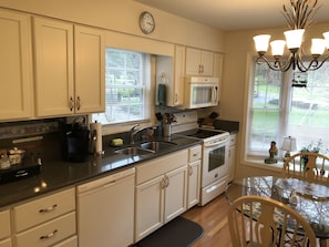 A kitchen with white cabinets, a microwave, a stove, a sink, and a dining area with a glass table and chairs.
