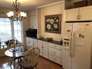 A kitchen with a dining table, chairs, a chandelier, a refrigerator, and a painting on the wall.